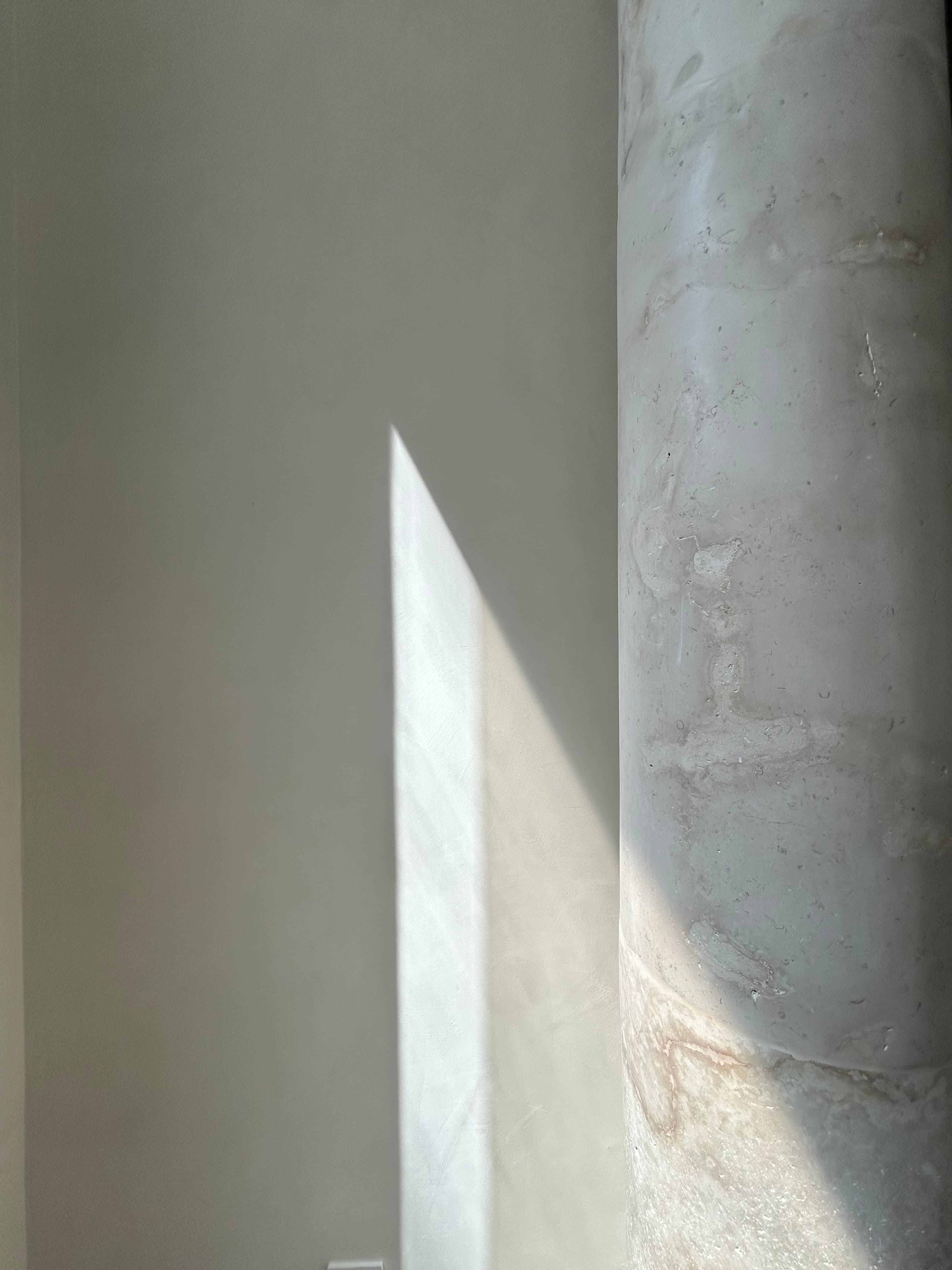 Light across mineral plaster beside a stone column